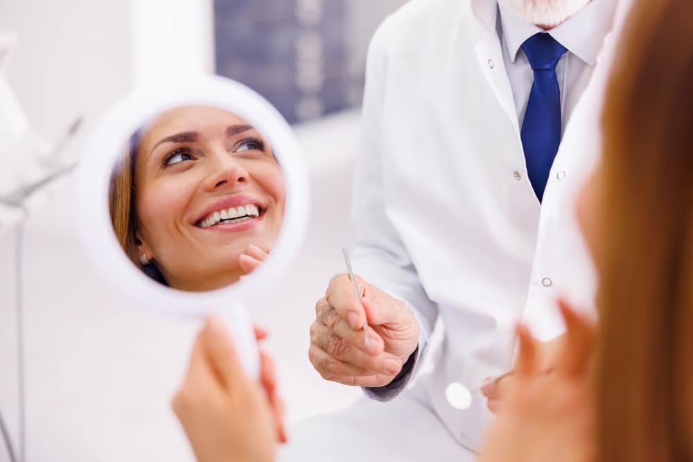 Woman,Looking,In,The,Mirror,And,Smiling,After,Checkup,At