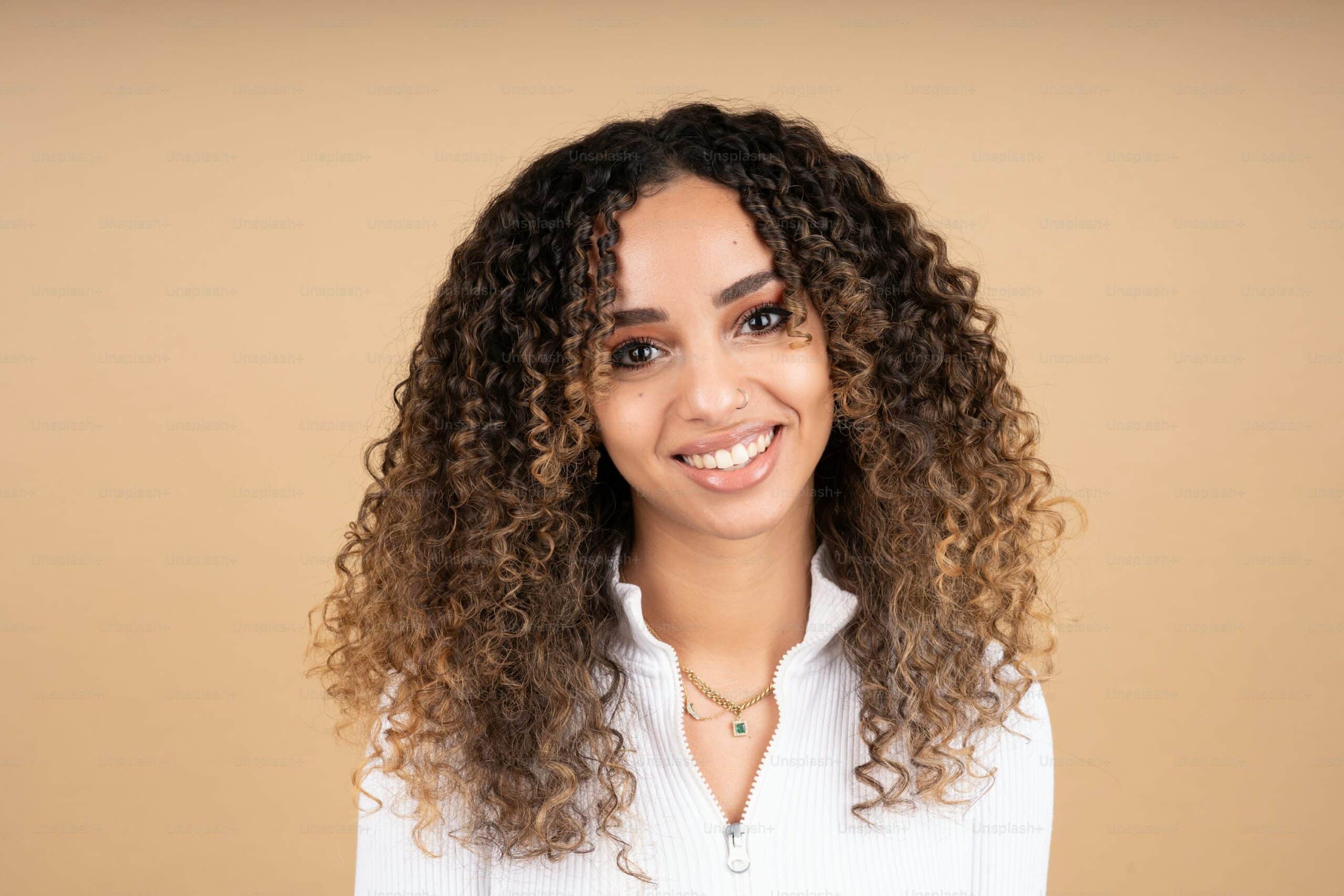 A woman with curly hair smiling and showing healthy, bright teeth, illustrating a natural-looking smile often associated with dental veneers.