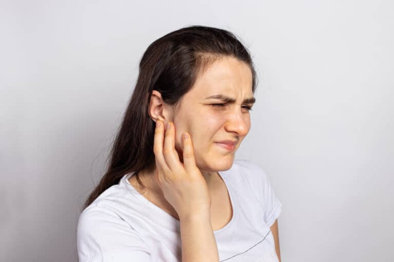 Person touching the side of their jaw with a pained expression, suggesting jaw discomfort or tension