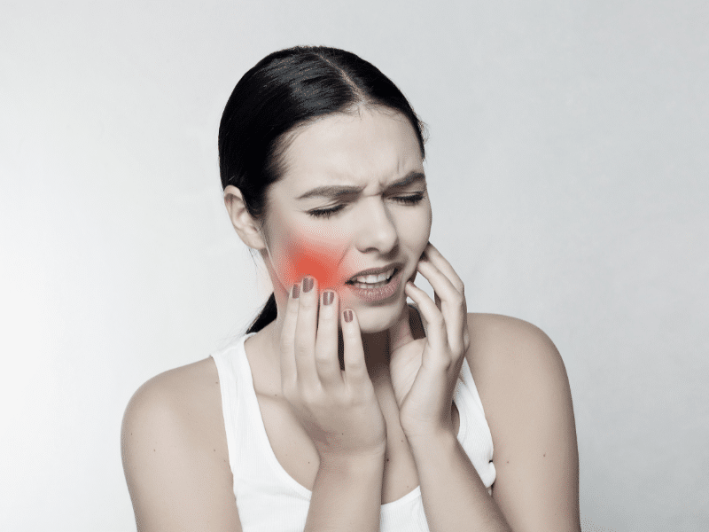 Woman holding her cheek with a painful expression indicating tooth pain