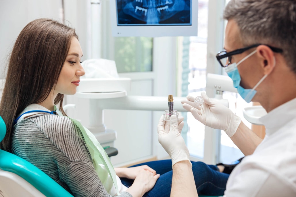 Dentist showing a dental implant model to a patient during a consultation and treatment planning appointment.