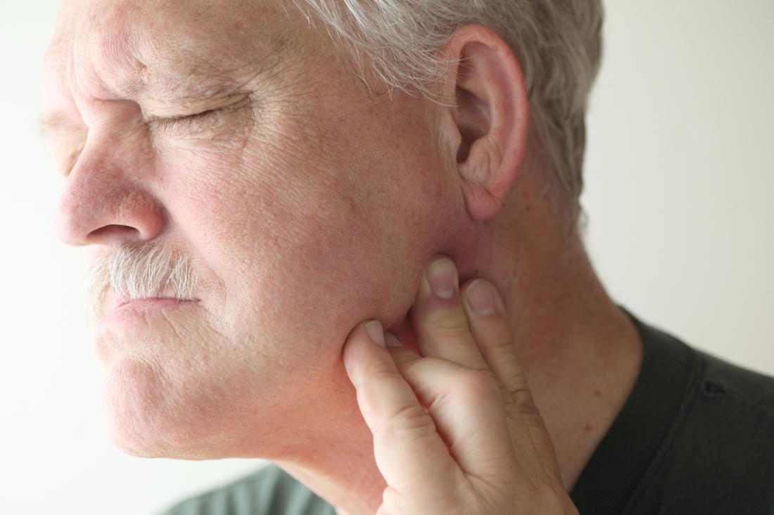 Older man pressing his jaw and cheek area while experiencing discomfort near the temporomandibular joint (TMJ).