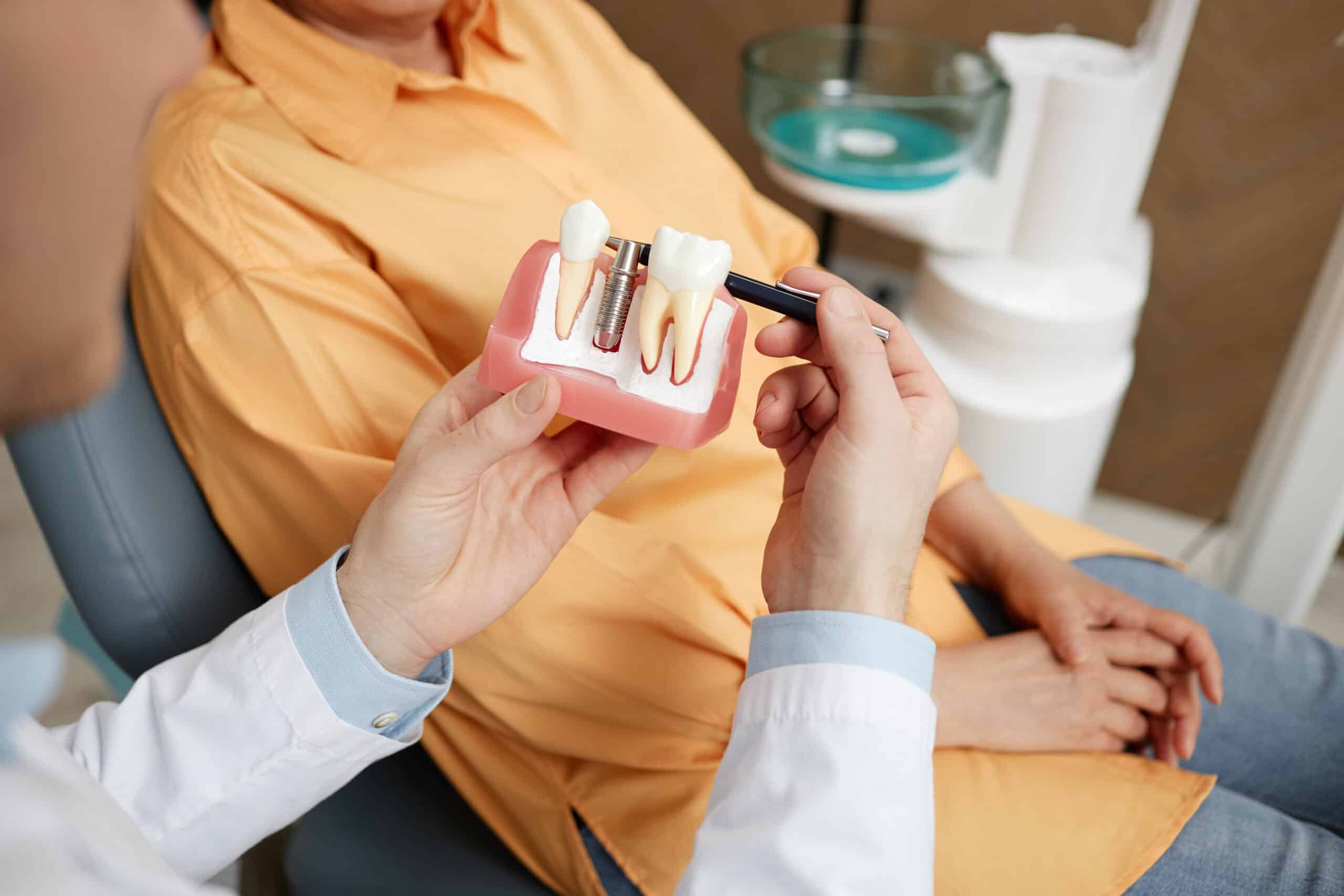 Dentist holding a dental implant model and pointing to the implant while explaining the treatment to a patient.