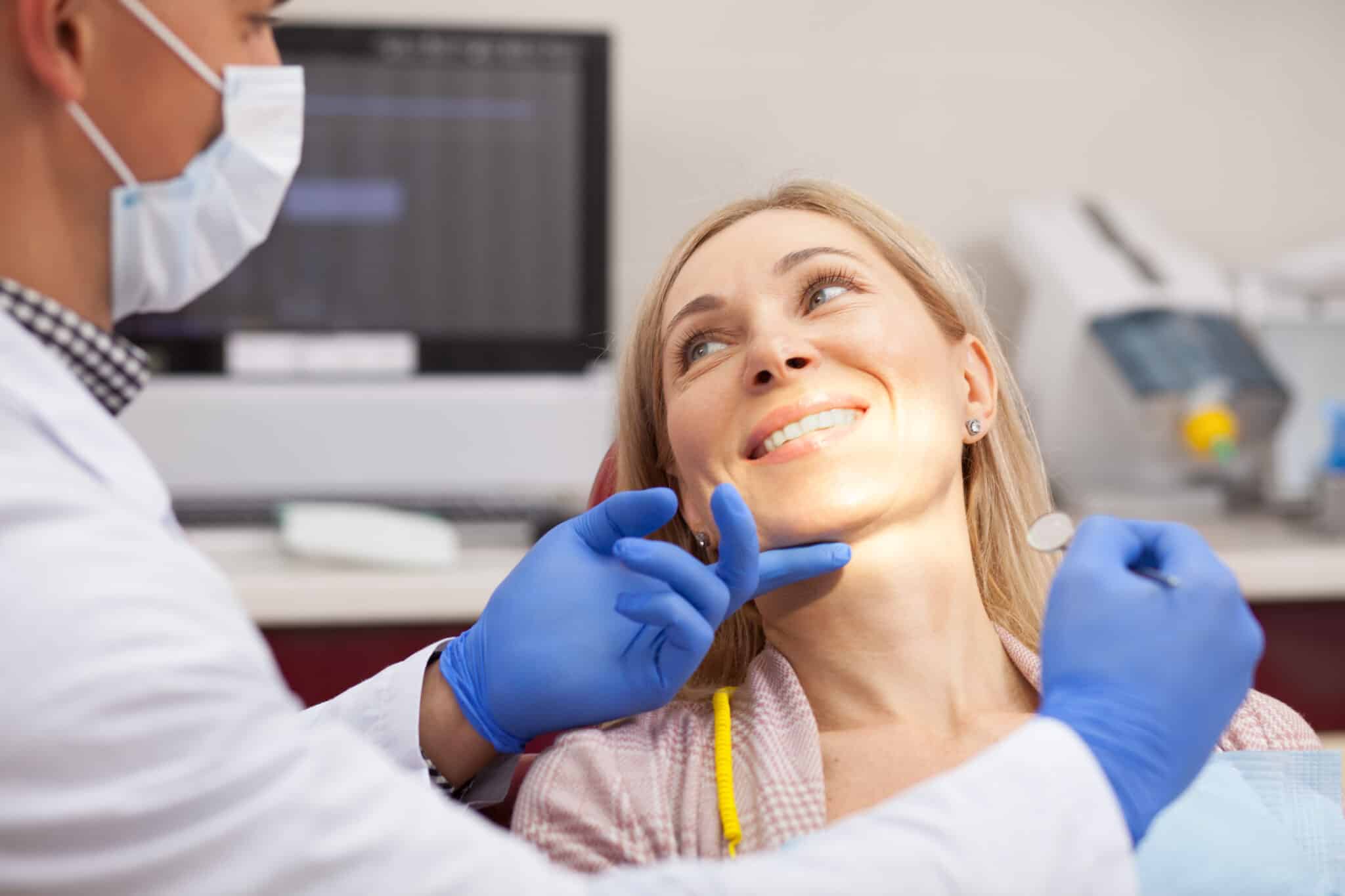 Dentist wearing gloves and a face mask examining a smiling patient during a routine dental checkup.