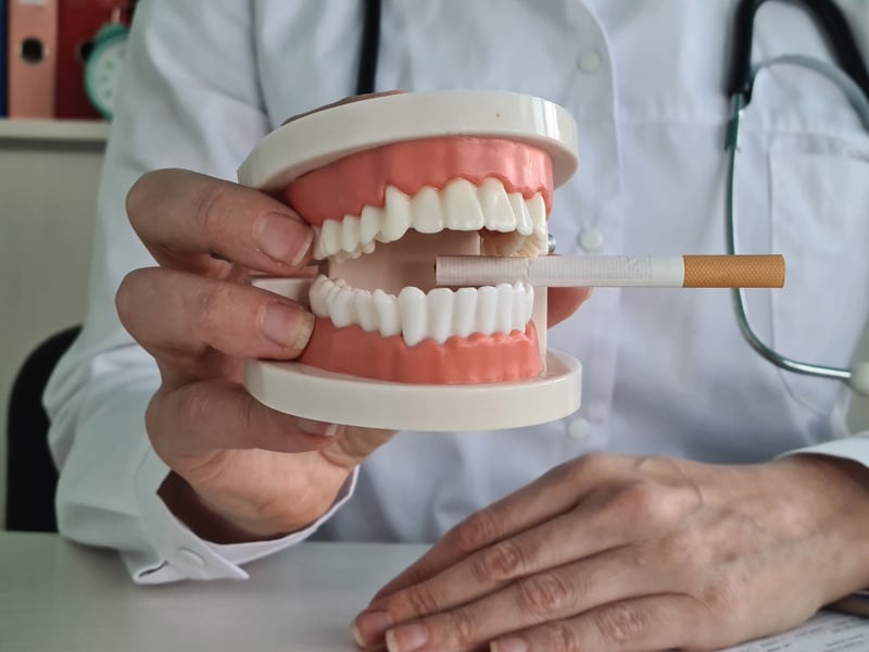 Dental professional holding a dental model with a cigarette placed between the upper and lower teeth.